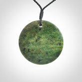 This piece is a large sized, oval round, disc pendant. It is suspended on a black coloured braided cord that is length adjustable.